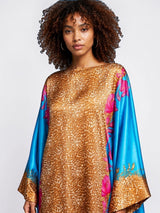 Model wearing an ALBANA New York aqua and gold satin kaftan with a mixed animal and floral print and wide sleeves.