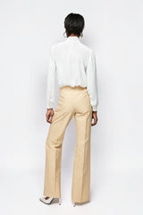 Model wearing ALBANA New York high-waisted beige pinstripe flare trousers with a white blouse, back view.