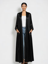 ALBANA New York black satin longline duster abaya with side pockets worn by a model over jeans and a white top