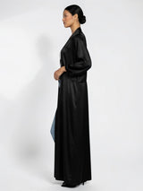 ALBANA New York black satin longline duster abaya with side pockets worn by a model in a side profile view.
