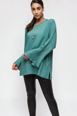 Model wearing ALBANA New York la mer blue textured linen tunic with wide sleeves and high neck, paired with leggings.