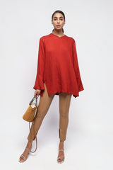 Model wearing an ALBANA New York coral red textured linen tunic with wide sleeves and side slits, paired with tan trousers.