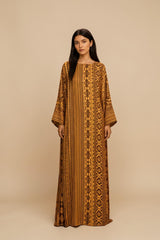 Model wearing an ALBANA New York Gilded Amber silk kaftan with wide sleeves and intricate tonal geometric patterns.