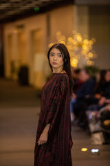 Model wearing an ALBANA New York Imperial Wine silk kaftan with a boat neckline and tonal patterned maroon fabric.