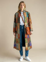 Model wearing an ALBANA New York long silk coat with a colorful mosaic pattern and noir trim over jeans and a tee.