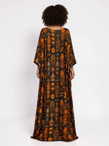 Model wearing ALBANA New York obsidian silk kaftan with orange heritage motifs, boat neckline, and flowing silhouette.