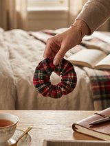 ALBANA New York mini tartan plaid scrunchie in red, green, and yellow woven cotton held by a hand in a cozy room.