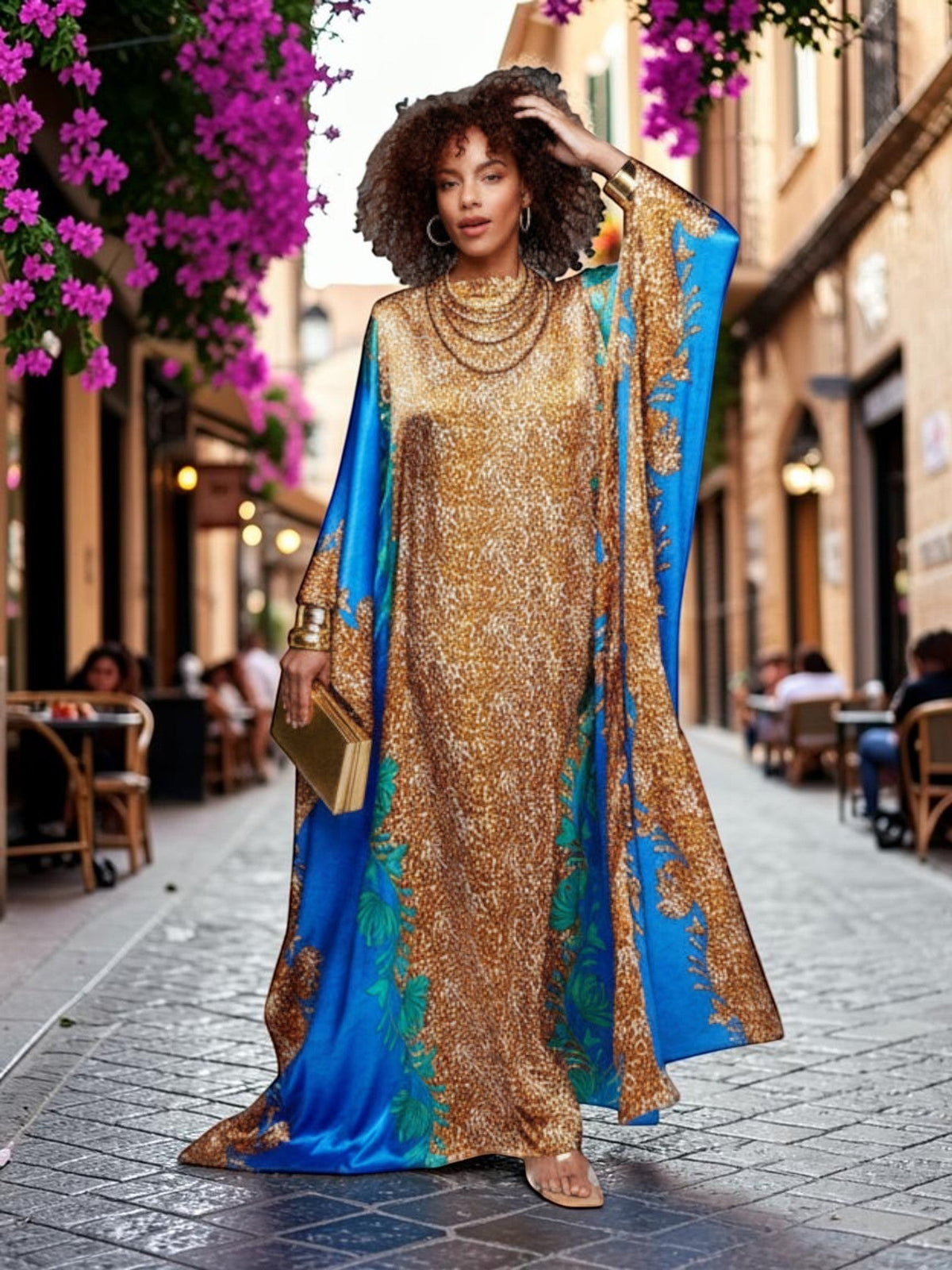 Model wearing an ALBANA New York azure blue and gold satin kaftan with intricate patterns on a cobblestone street.