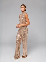 Model wearing ALBANA New York gold sequin sleeveless mock neck blouse and matching wide-leg sequin trousers.