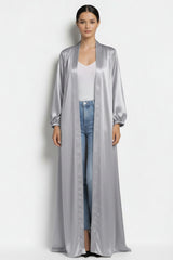 ALBANA New York gray satin duster abaya with long sleeves and gathered cuffs worn over a white top and jeans.
