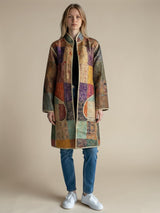 Model wearing an ALBANA New York longline silk coat with a colorful mosaic pattern, open front, and gold trim.
