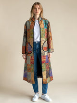 Model wearing ALBANA New York long silk coat with mosaic pattern, noir trim, and pockets over jeans and white sneakers.