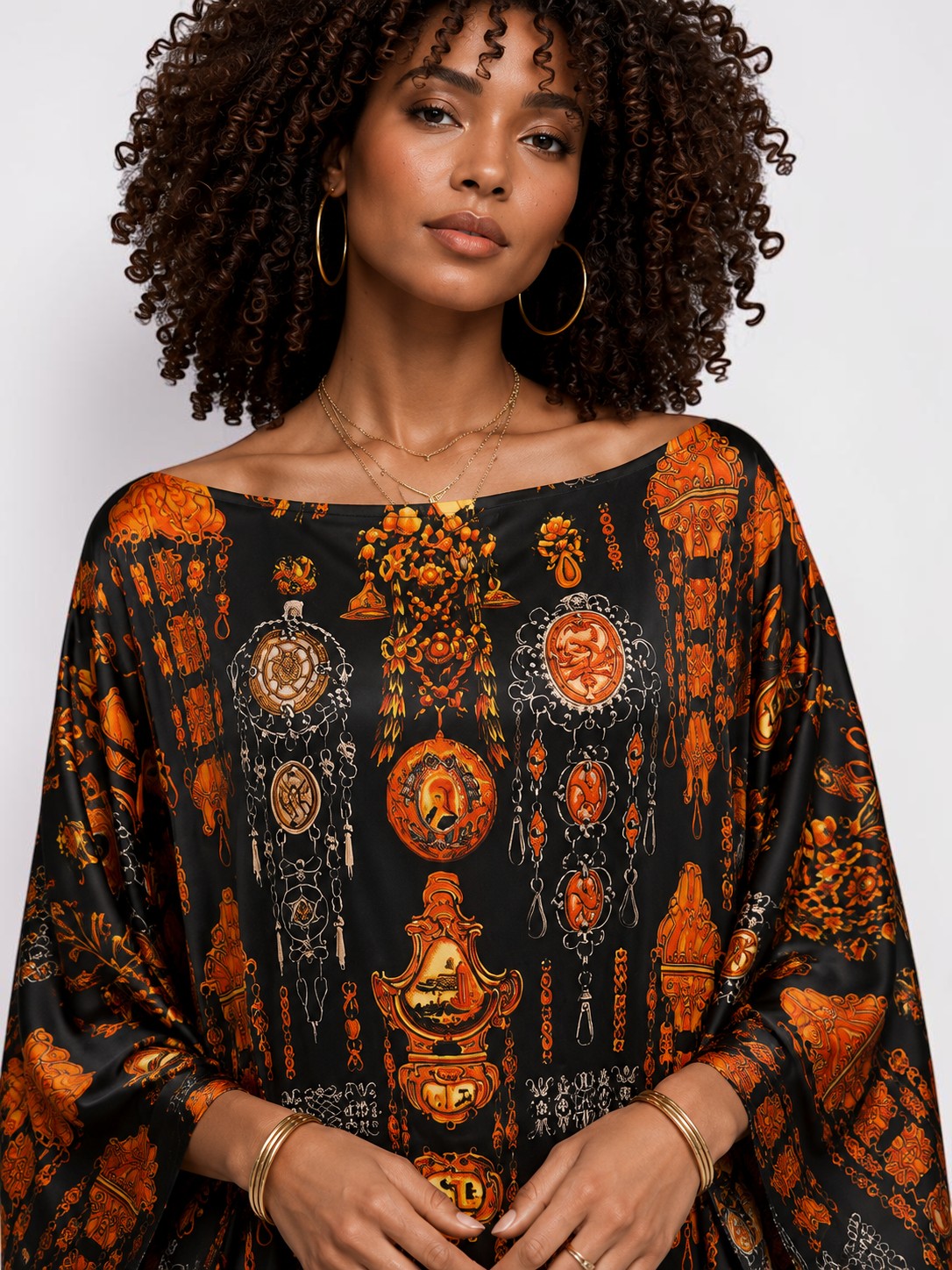 Model wearing an ALBANA New York obsidian silk kaftan with an intricate orange heritage motif and boat neckline.