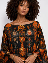 Model wearing an ALBANA New York obsidian silk kaftan with an intricate orange heritage motif and boat neckline.
