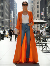 ALBANA New York orange satin maxi duster abaya worn over a white tank top and blue jeans on a city street.