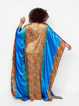 Model wearing ALBANA New York Sahara Azure satin kaftan with vibrant blue and gold leopard print and flowing wide sleeves.