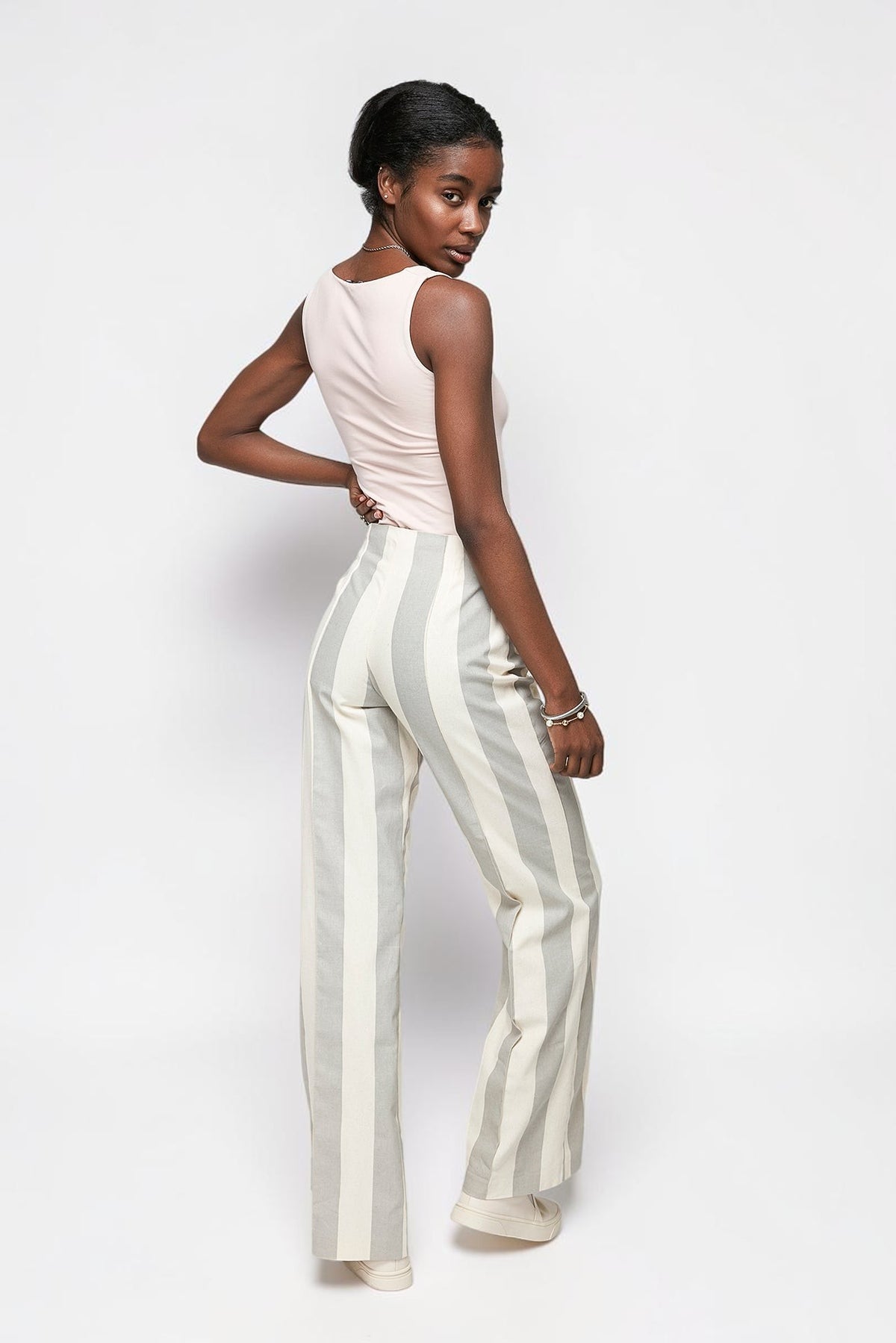 Model wearing ALBANA New York cotton flare pants with vertical stripes and double pleats, back view.